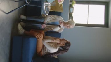 Oturma odasındaki kanepede beyaz saçlı son sınıf öğrencisiyle konuşan kadın asistanın dikey görüntüsü.