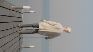 Dikey olarak yaşlı bir kadının tahta iskelede yürüdüğü ve gölde şafak sökerken güzel bir görüntüsü.