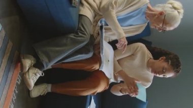 Yaşlı bir kadının finansal çalışma kitabını tutarken ve hesap makinesi kullanırken gündüz evde kadın sosyal hizmetler görevlisinin yardımıyla faturaları sayarken dikey karesi.