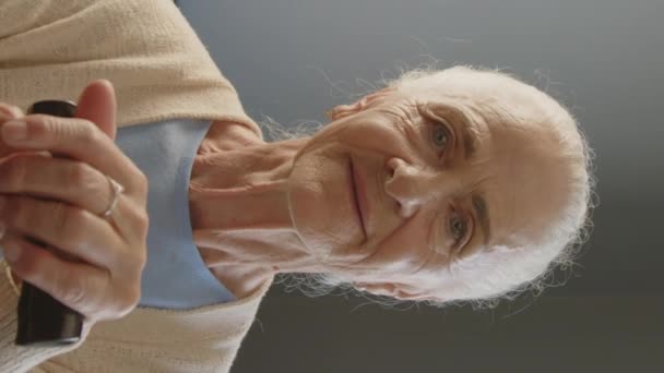 自宅に座っている間 杖を歩いてカメラを見ている灰色の髪を持つ高齢女性の垂直な肖像画 — ストック動画