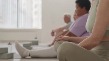 Yetişkin bir kadının grup çalışması sırasında yoga stüdyosunda bacak bacak bacak üstüne atarak oturduğu seçici odak fotoğrafını çek.