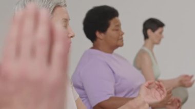 Stüdyoda yoga yaparken Namaste 'de gözleri kapalı meditasyon yapan ve elleri kapalı bir grup son sınıf kadınını aşağı doğru çek.