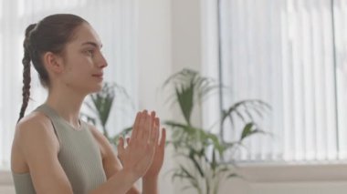 Namaste 'de elleri ve gözleri kapalı yoga meditasyonu yapan genç bir kadının orta boy fotoğrafı.