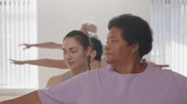 Genç bayan yoga öğretmeni kıdemli Afrikalı Amerikalı kadına yardımcı oluyor. Spor salonunda grup çalışması sırasında savaşçı pozu veriyor.