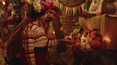 Arka bahçede Dia de Muertos 'u kutlarken büyükannesinin mihrabında dikilen saçında çiçek çelengi olan Meksikalı küçük bir kızın orta boy fotoğrafı.