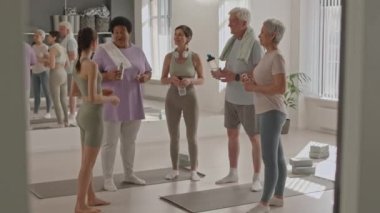 Yoga stüdyosunda duran ve su molası sırasında konuşan bir grup çok ırklı son sınıf öğrencisi ve genç bayan fitness eğitmeni.