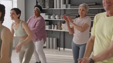 Spor giyim bölümündeki üst düzey kişiler, stüdyoda spor koçu ile antrenman yaparken el çırpmalarıyla aerobik egzersizi yapıyorlar.