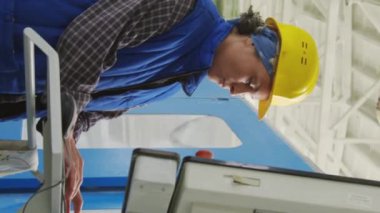 Fabrikada çalışan kadın teknisyen ve sanayi makinesinin dikey görüntüsü.
