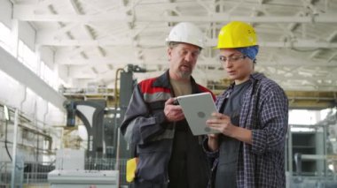 Erkek ve kadın iş arkadaşlarının taş kesme fabrikasındaki makineleri incelerken telsiz ve dijital tablet kullandıkları orta boy bir fotoğraf.