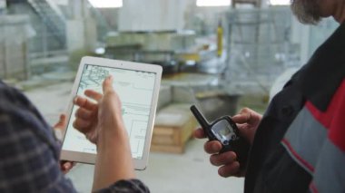 Erkek ve kadın mühendislerin dijital tablete yakınlaştırılmış çalışma kıyafetleri ve mermer fabrikasında üretim işlemleri tartışmaları.