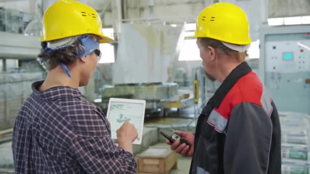 戴硬帽和制服的男男女女同事在工厂一起工作一段时间后在数字平板屏幕上讨论计划 — 图库视频影像