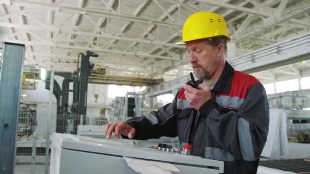 工場で産業機械を操作しながら ウォルキー トーキーを使用したハード ワークウェアの経験豊富な男性エンジニアの中型ショット — ストック動画