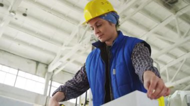 Taş fabrikasındaki mermer levhanın uzunluğunu ve genişliğini ölçmek için mezura ve iş kıyafetleri kullanan kadının düşük açılı görüntüsü
