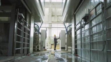 Taş fabrikasında çalışan ve endüstriyel makineleri çalıştıran iş kıyafetleri teknisyeninin geniş açılı görüntüsü.