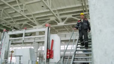 Dijital tabletle kasketli ve iş kıyafetli bir erkek müfettiş ve sanayi fabrikasında merdivenlerden aşağı iniyor.