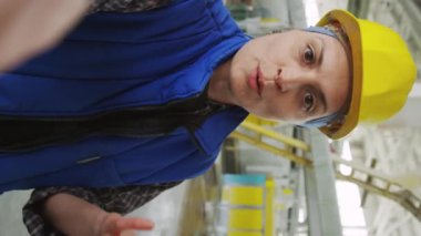 Dikey olarak kadın mühendis kameraya bakarken ve endüstriyel fabrikadaki iş günlerini anlatırken video araması veya video kaydı yaparken.