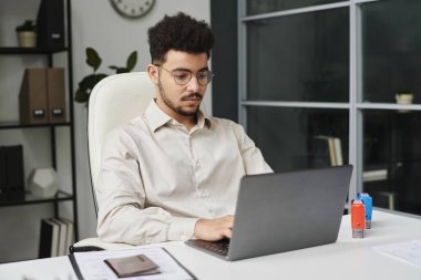 Genç işadamı işyerinde oturuyor ve vize merkezinde dizüstü bilgisayarla çalışıyor.