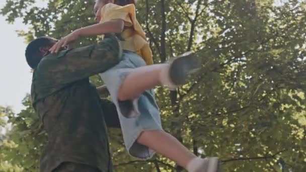 从低角度慢镜头拍摄的爱着身着战斗服的非裔美国爸爸在服役归来的路上 提起并旋转着兴奋的小女儿在公园里 — 图库视频影像