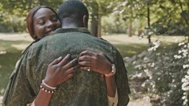 Neşeli bir Afrikalı Amerikalı kadın askeri üniformalı kocasını kucaklıyor ve mezuniyet balosundan sonra onunla buluşurken mutlu bir şekilde gülümsüyor.