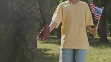 Afro-Amerikalı küçük bir kızın Amerikan bayrağını tutarken ve askerî üniformalı babasıyla el ele tutuşurken görüntüsü.