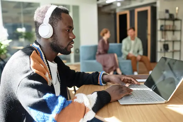 African American businessman in wireless headphones working online on laptop while sitting in office hall