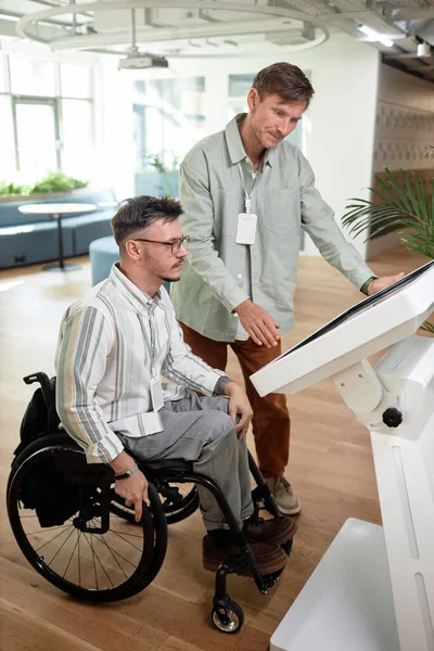 Vertical image of man helping to make online entry for man with disability in office hall