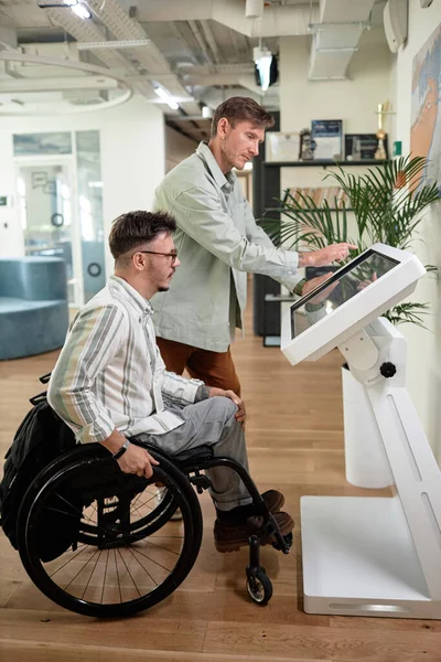Vertical image of man with disability using computer monitor in office with businessman