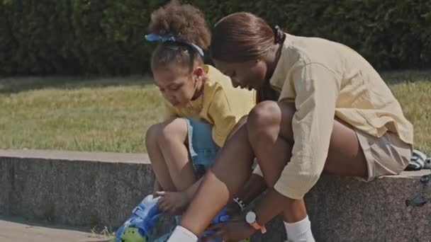 Afrikansk Amerikansk Flicka Sitter Trottoarkanten Parken Och Sätta Rullskridskor Med — Stockvideo