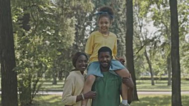 Yazın parkta mutlu bir Afrikalı Amerikalı ailenin portresi, babasının omzunda oturan küçük bir kız.