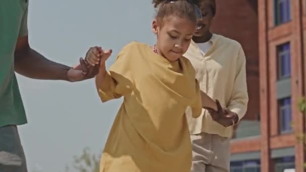 当她第一次在户外滑板时 中镜头是快乐的非洲裔美国母亲和父亲牵着小女儿的手 — 图库视频影像