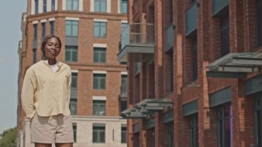 Orta boy, Afro-Amerikan bir kadının sokakta dikilip kameraya bakıp güneşli bir günde mutlu mesut gülümsediği bir fotoğraf.