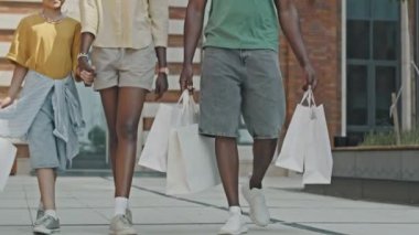 Afrika kökenli Amerikalı bir kadının küçük kızıyla el ele tutuşurken ve kocasıyla sohbet ederken aile alışverişinden sonra birlikte yürürken çekilen yavaş çekim.