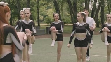 Bir grup ponpon kız futbol sahasında antrenman yaparken diz göğüse antrenman yapıyorlar.