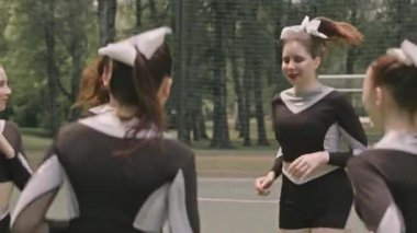 Dışarıda futbol sahasında ısınma egzersizi yaparken üniformalı genç ponpon kızlardan oluşan kavisli bir fotoğraf.