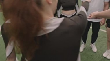 Ponpon kızlardan oluşan 360 derecelik bir takım ellerini birleştiriyor ve sonra da futbol sahasında el ele tutuşurken kollarını kaldırıyor.