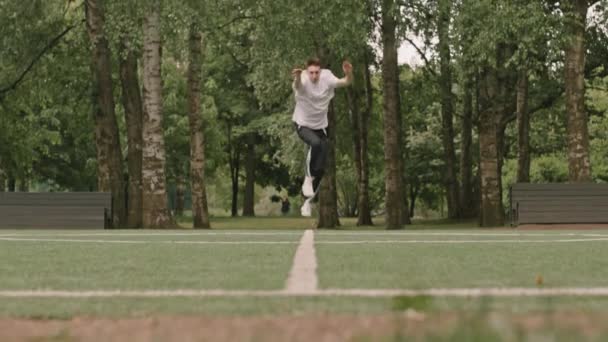 屋外のサッカー場で運動しながら カートホイールとバックフリップを行う若いアスリートのワイドショット — ストック動画