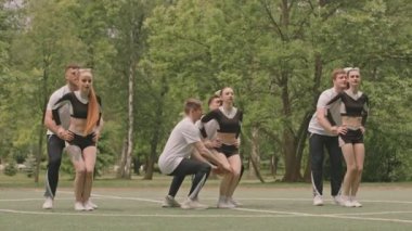 Açık hava spor sahasındaki ponpon kız gösterilerinde topuk esneme hareketi yapan güçlü erkek sporcuların el ilanı kızlarını havada tutarken çekimini yapın.