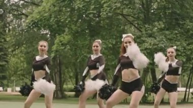 Spor üniformalı, ponpon kızlarla dans eden ve açık hava futbol sahasındaki performansı sırasında kameraya gülümseyen genç bayan amigo takımı.