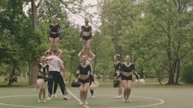 Ponponlarla dans eden ve açık hava futbol sahasında dans eden bir grup ponpon kız.