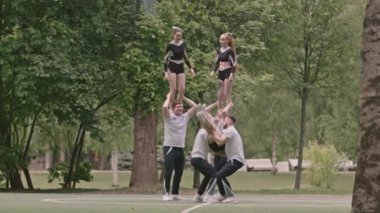 Açık hava spor sahasında birlikte antrenman yaparken, ponpon kız takımının piramit dublörlüğü çalışması geniş bir açı.