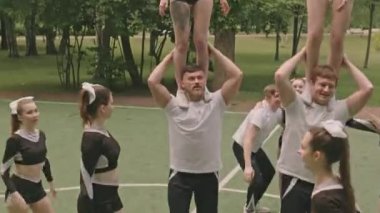 Bir grup erkek ve kadın amigo piramit yapıyor, sonra gülüyorlar ve açık hava futbol sahasında birbirlerine beşlik çakıyorlar.