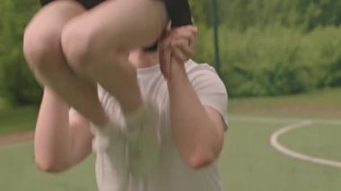 Spor sahasında amigoluk yaparken kaslı sporcu el ilanı taşıyan kızı kaldırıyor ve başının üstünde tutuyor.