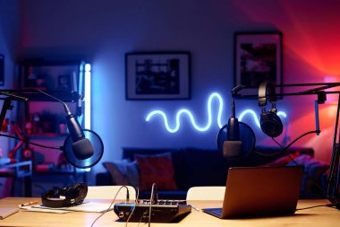 Laptop kulaklıklı mikrofonlarla çevrili ve stüdyodaki modern radyo sunucusunun çalışma yerinde duruyor.