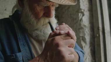 Kapalı alanda dinlenirken şapka piposu giyen yaşlı sakallı adama yaklaş.