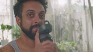 Şişeden su içen ve evde egzersiz yaptıktan sonra kameraya bakan sakallı adamın göğüs portresi.