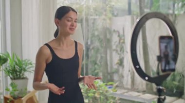 Kadınların vlog çekerken ya da evde sosyal medyada canlı yayın yaparken akıllı telefonun önünde tripodla abone olan abonelerle el sallayıp konuştuğu orta boy bir görüntü.