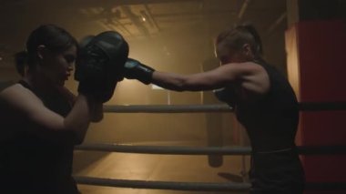Güçlü bir kadın boks ringini yumruklarken kadın eğitmenin orta boy bir fotoğrafı.