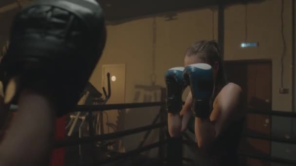 リングでのワークアウト中にパンチダットを身に着けている女性トレーナーをパンチするボクサーのサイドビュー — ストック動画