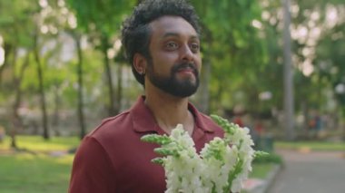 Romantik bir adamın gülümsemesi ve sevgili kız arkadaşını selamlaması, parkta buluşurken ona bir buket çiçek ve kahve vermesi.