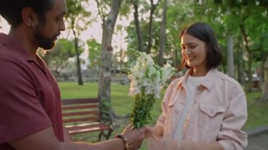 Genç adamın sevgilisine bir buket çiçek verirken ve gün batımında parkta romantik bir randevuda ona sarılırken.